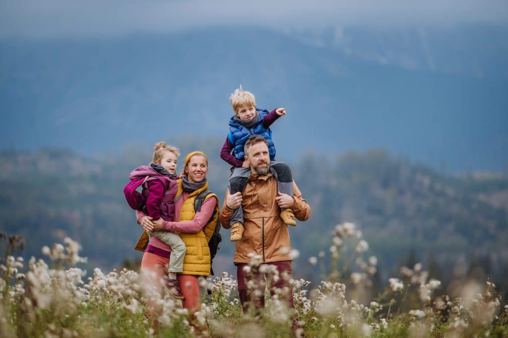 Happy parents with their little kids on piggyback at autumn walk.