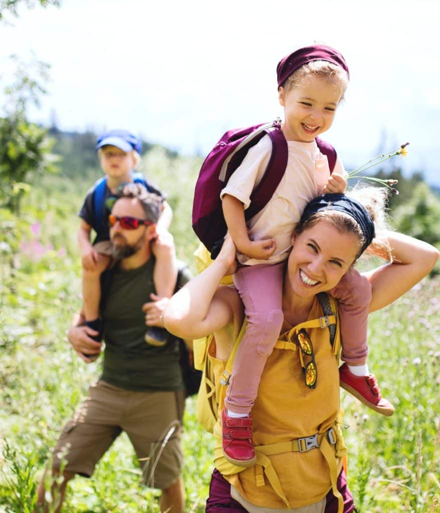 Happy parents with their little kids on piggyback at summer walk.