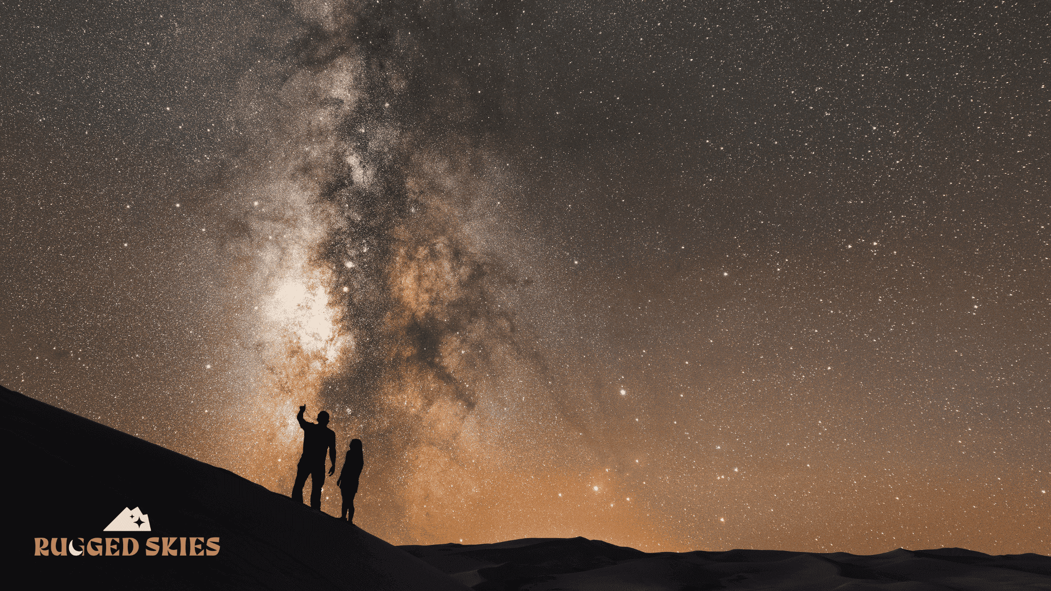 Two stargazers staring out at a vivid, yellow-tinted milky way galaxy